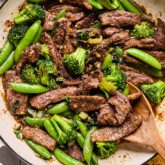 Honey garlic beef stir fry in a pan with a wooden spoon.