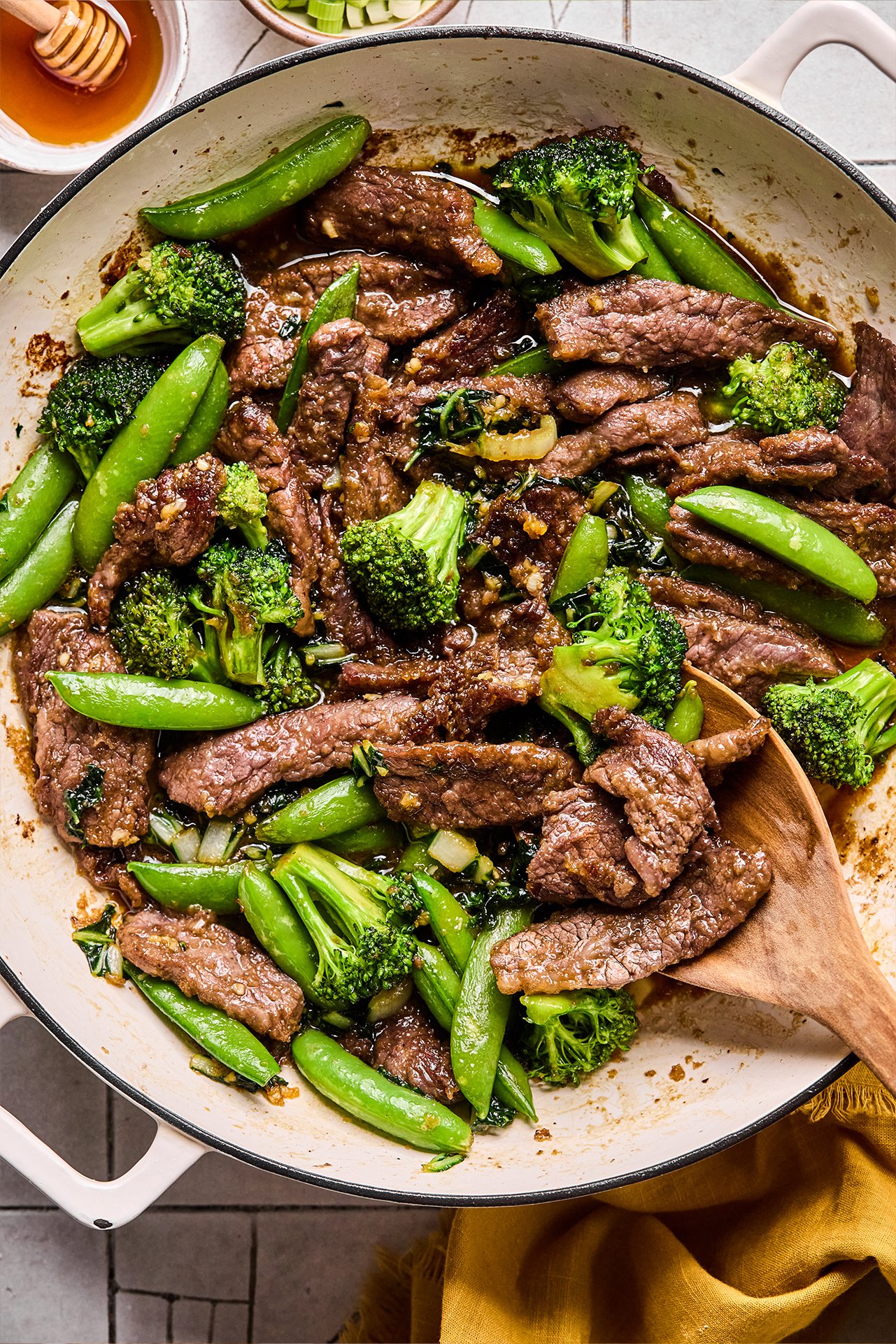 Honey garlic beef stir fry in a pan with a wooden spoon.