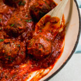 Wooden spoon scooping an Italian lamb meatball from a pan.