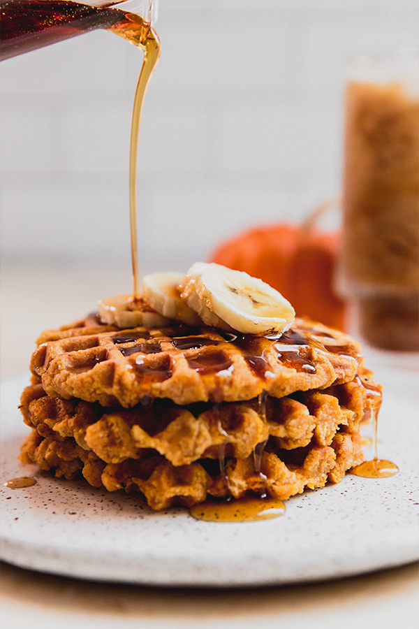 A stack of pumpkin waffles with banana and maple syrup on it.