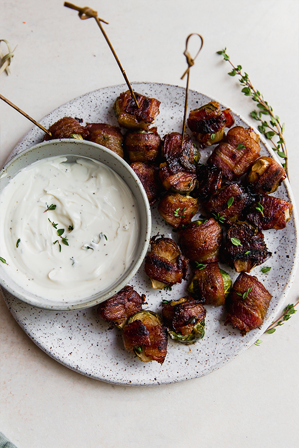 A platter with bacon wrapped brussels sprouts and dipping sauce.