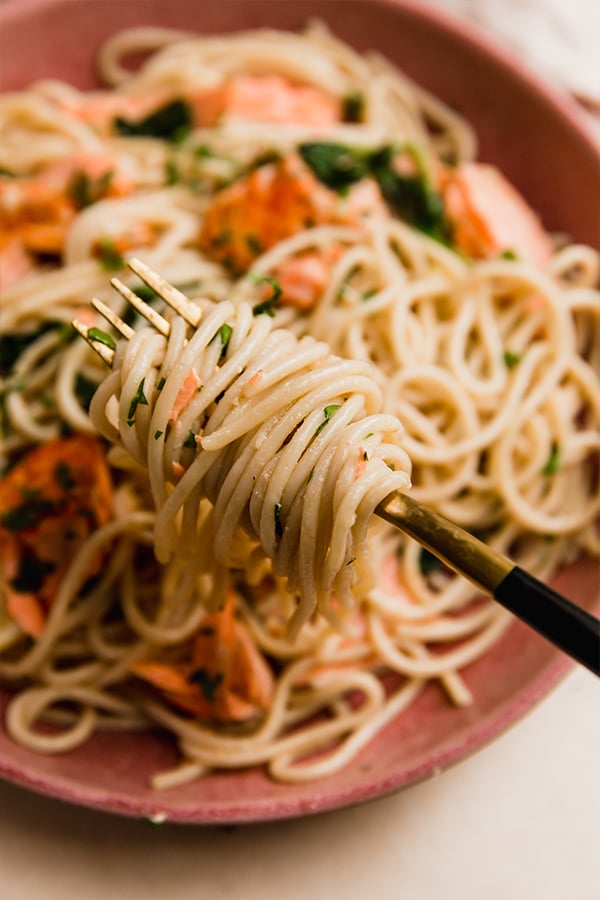 A bowl of lemon salmon pasta with a fork taking a bite.