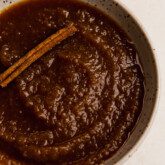 Slow cooker apple sauce topped with a cinnamon stick.