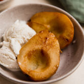 Two baked pear halves in a bowl with ice cream.