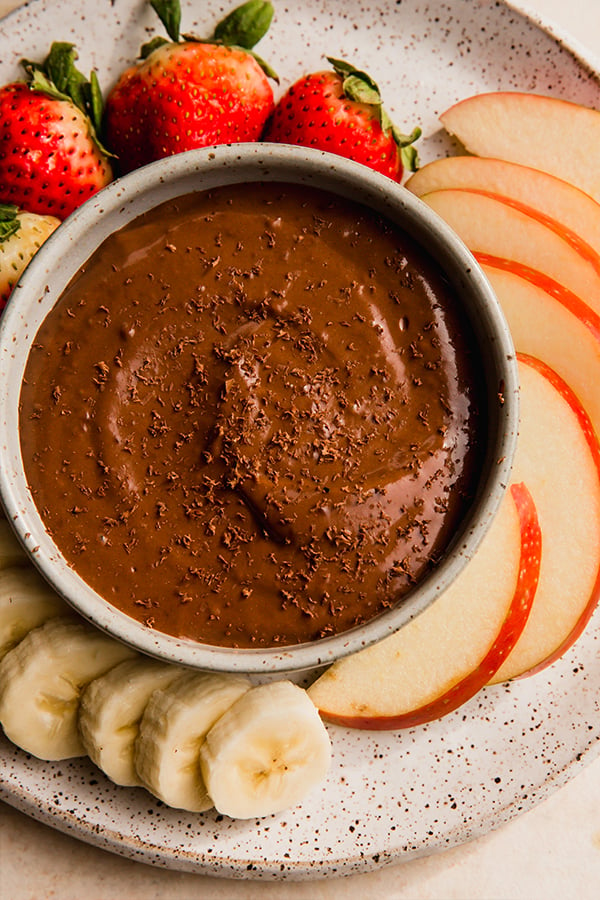 A bowl of chocolate fruit dip with fruit for dipping.