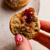 Person holding a jelly donut hole with a bite missing.