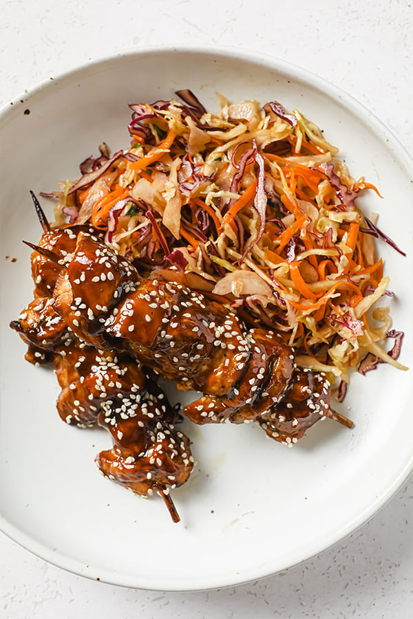 A plate with teriyaki chicken skewers and asian slaw.
