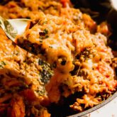 Scoop scooping dairy-free "cheesy" beef and sweet potato skillet from a pan.