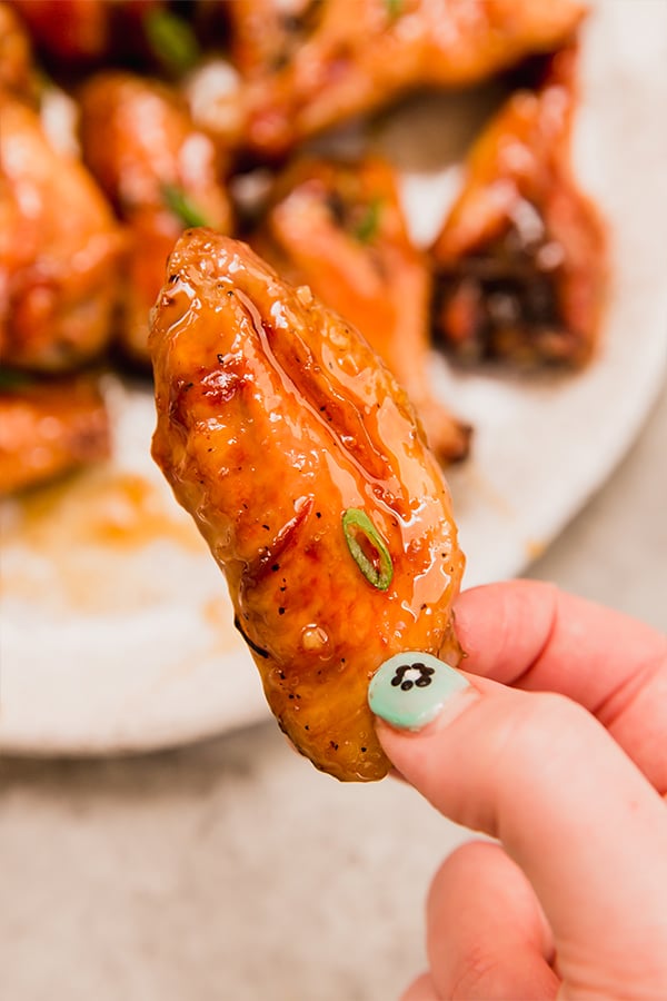 A baked honey-garlic chicken wings being held in a hand.