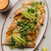 Baked ground beef tacos on a platter topped with avocado.