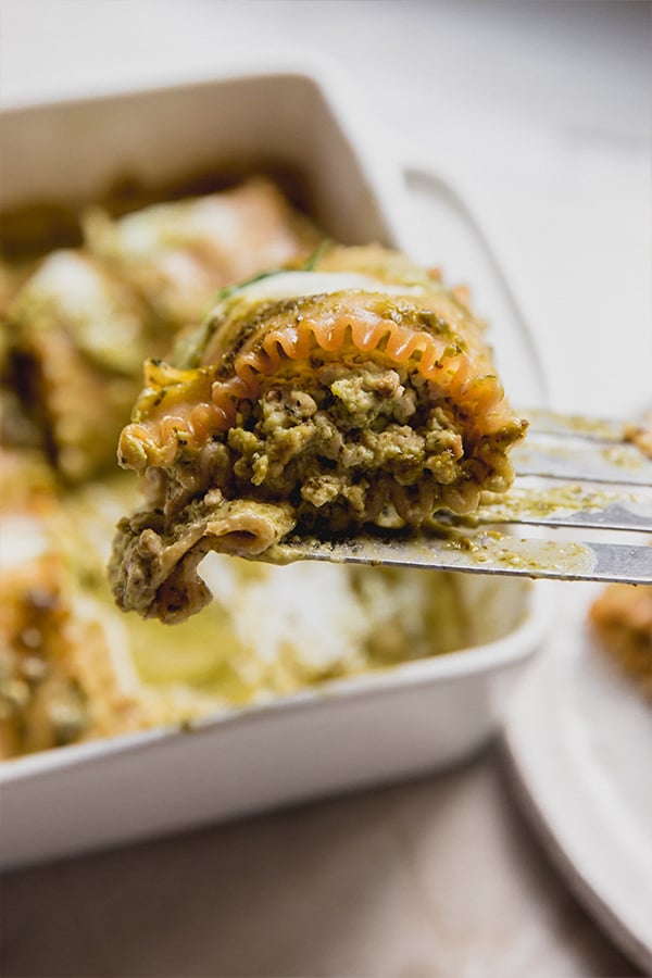 A spatula pulling out a serving of white pesto lasagna roll-ups from a casserole dish.