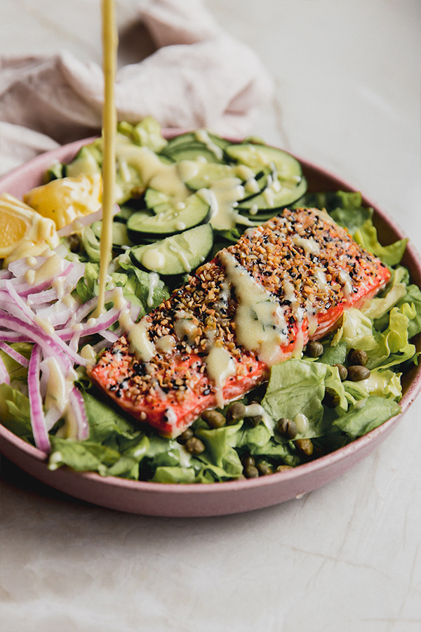 A bowl of the everything bagel salmon salad with dressing being poured on top.