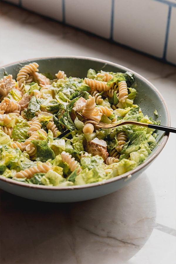 A bowl of chicken caesar pasta salad with a fork in it.