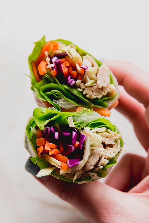 A chicken and vegetable spring roll cut in half being held in a hand.