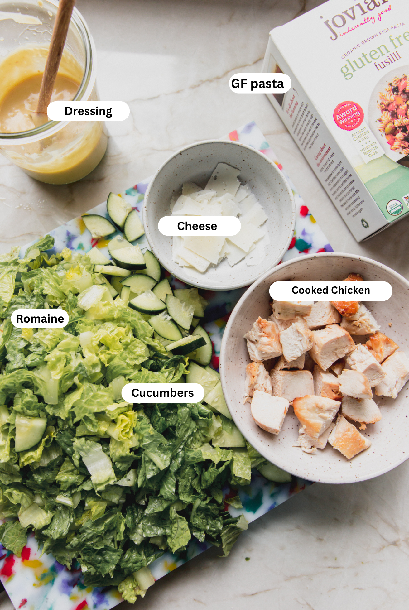 Caesar pasta salad ingredients laid out on a cutting board and in bowls