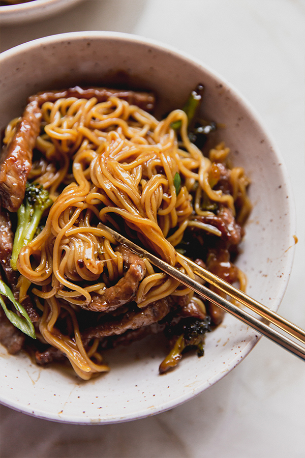 A bowl of sheet pan Mongolian beef in a bowl with chop sticks taking a bite out of it.