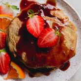 Strawberries on a stack of pancakes with orange syrup.