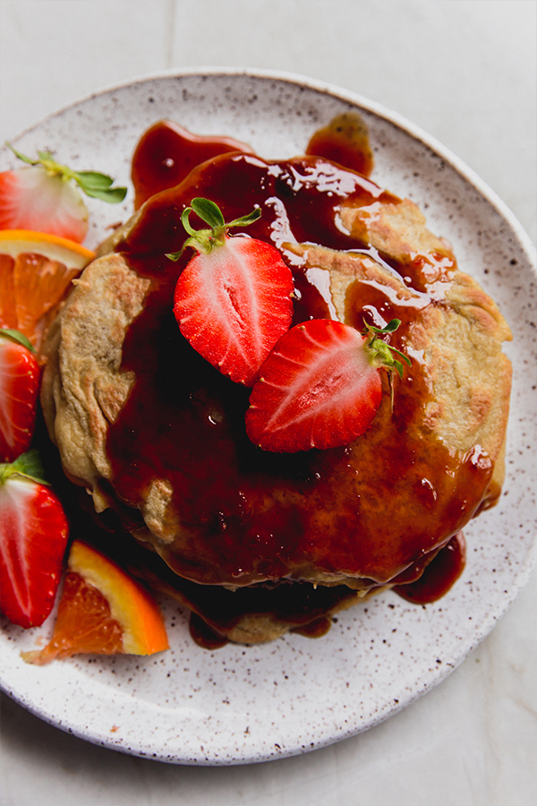 A plate of gluten-free pancakes with orange syrup and strawberries on a plate.
