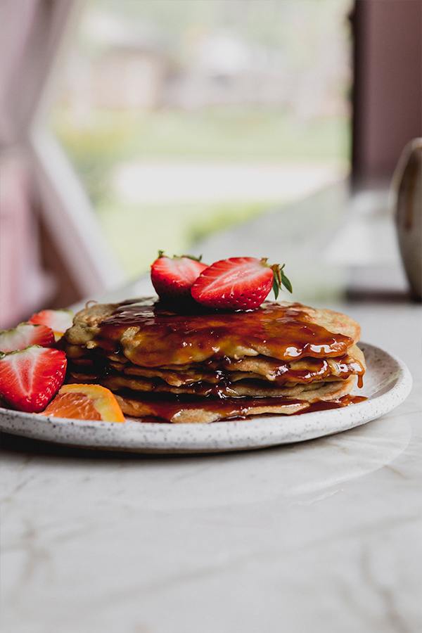 A stack of gluten-free pancakes with orange syrup and slice strawberries on it.