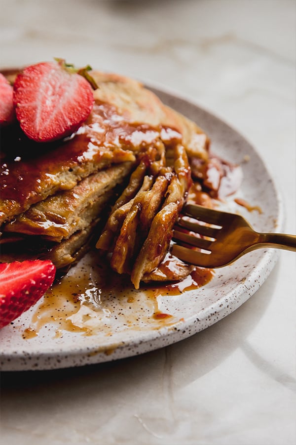 A stack of pancakes with orange syrup with a fork taking a bite.