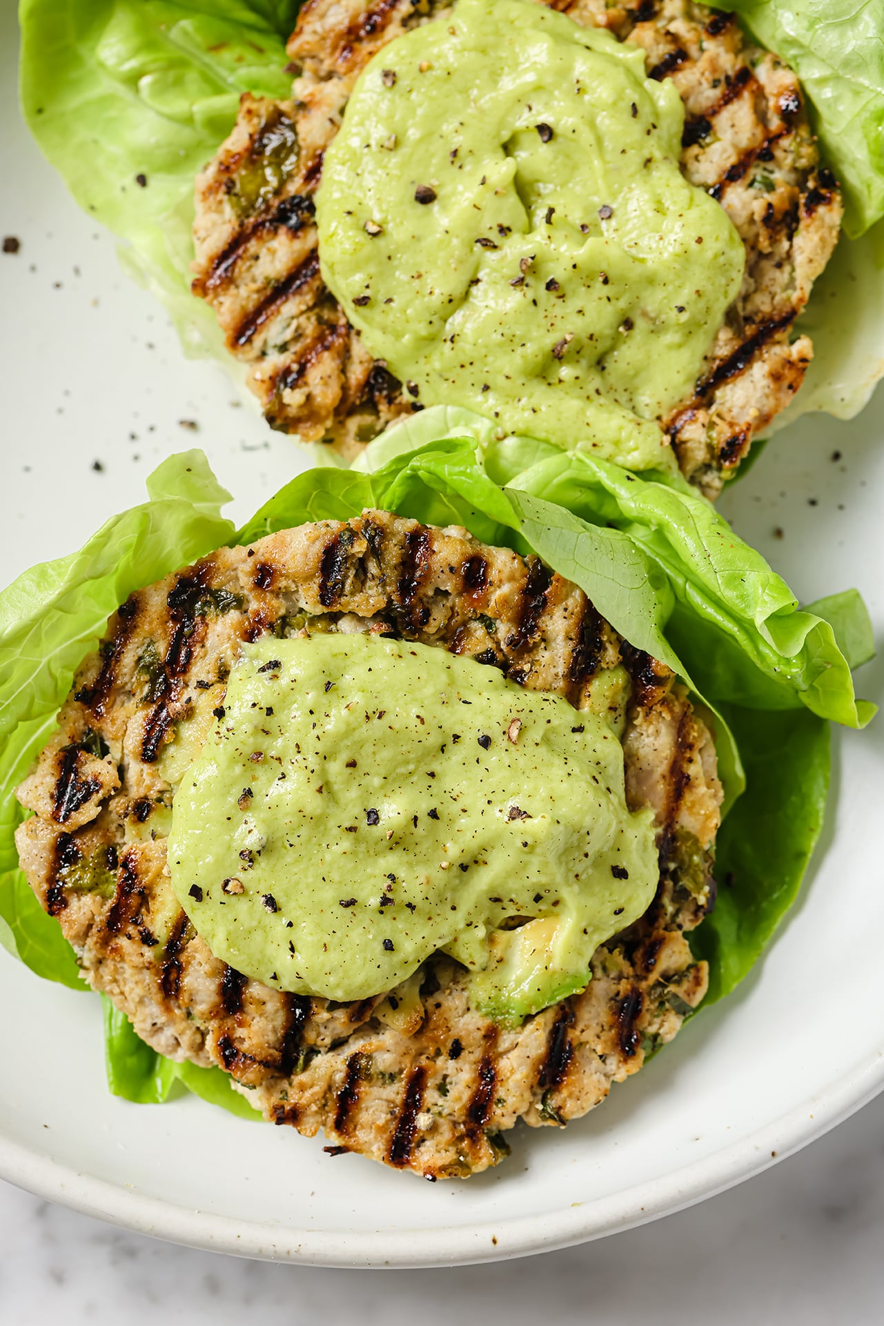 Two avocado chicken burgers topped with avocado mayo. 