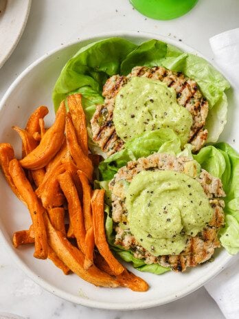 Avocado chicken burgers topped with avocado spread with a side of sweet potato fries.
