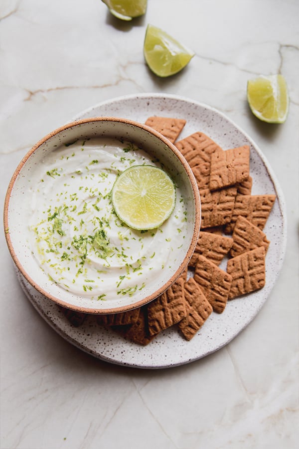A bowl of key lime pie dip surrounded by graham cracker pieces. 