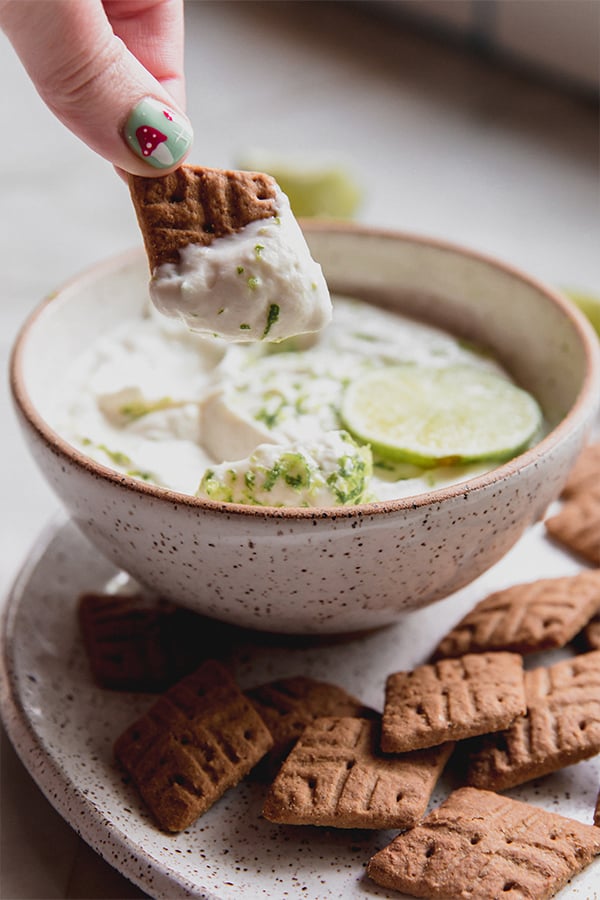 A graham cracker dipping into a bowl of key lime dip.