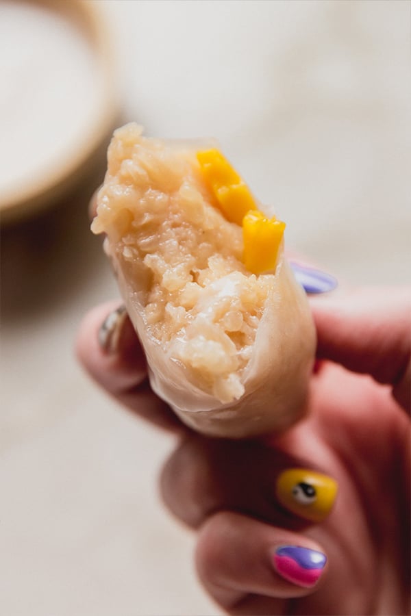 A mango sticky rice rolls being held in a hand with a bite taken out of it.