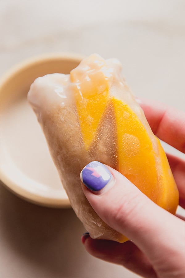 A mango sticky rice roll being held in a hand.