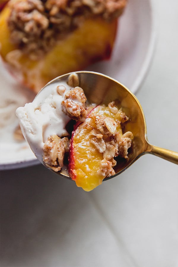 A bite of air fryer peach crisp and dairy free ice cream on a spoon.
