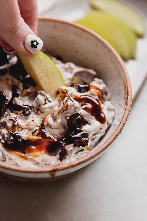 A bowl of snickers salad dip with an apple dipping into it.