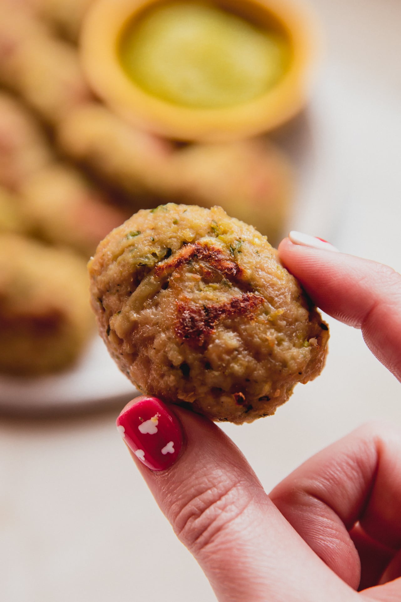 A hand holding one zucchini chicken nugget between the fingers.