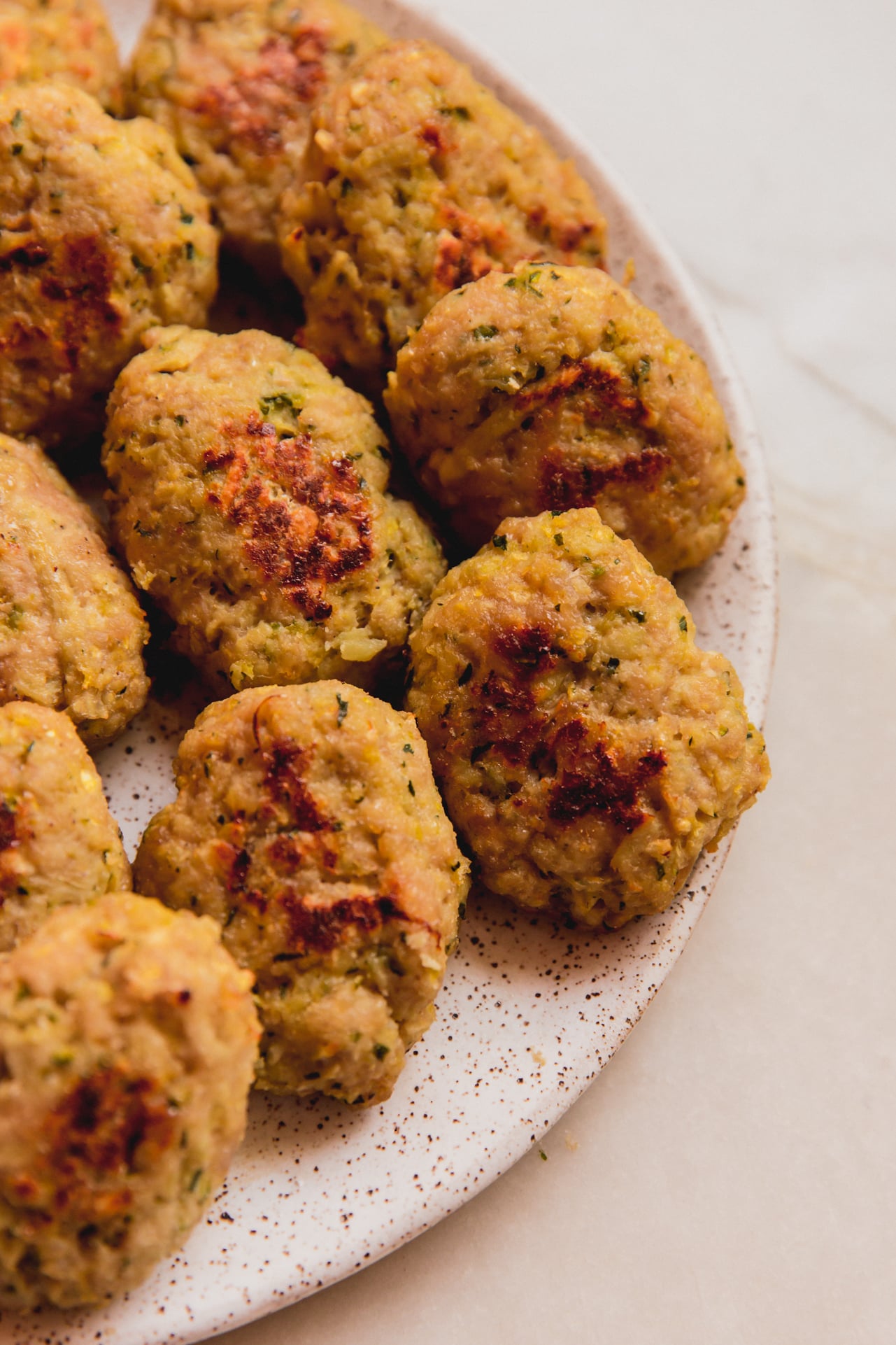 A white speckled plate with zucchini veggie chicken nuggets on it.