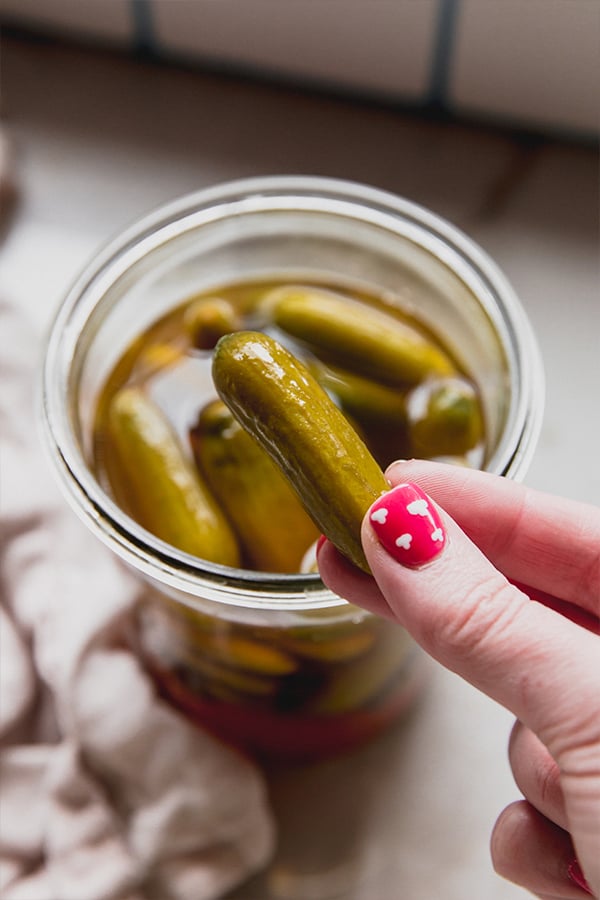 A hand picking up an apple cider vinegar pickle out of a jar.