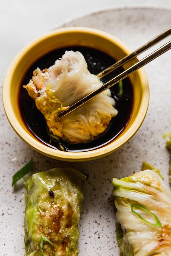 Chopsticks dipping a cabbage roll dumpling into coconut aminos.