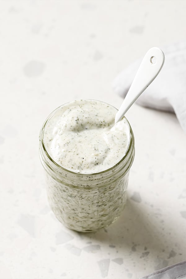A glass jar full of homemade ranch dressing to use in bacon ranch bow-tie pasta salad.