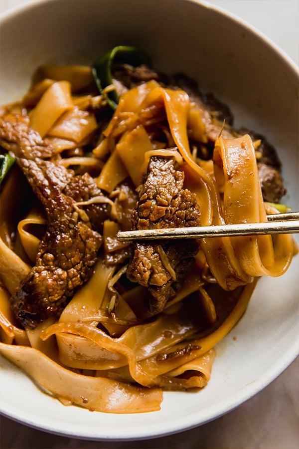 A bowl of beef chow fun with chopsticks taking a bite out.