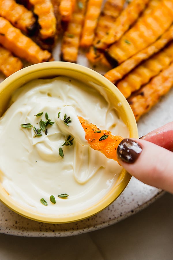 A platter of butternut zig zag fries with one fry dipping into the dipping sauce.