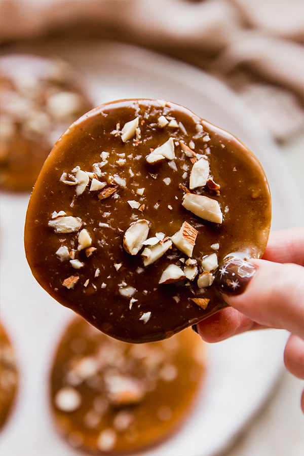 A caramel apple slice covered in crushed almonds and being held in a hand.
