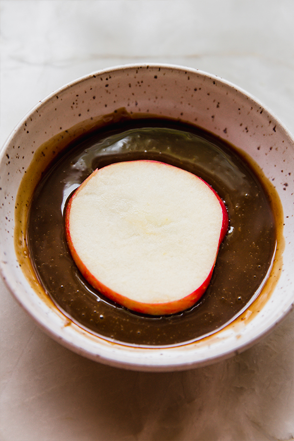 A apple slice being dipped into coconut milk caramel.
