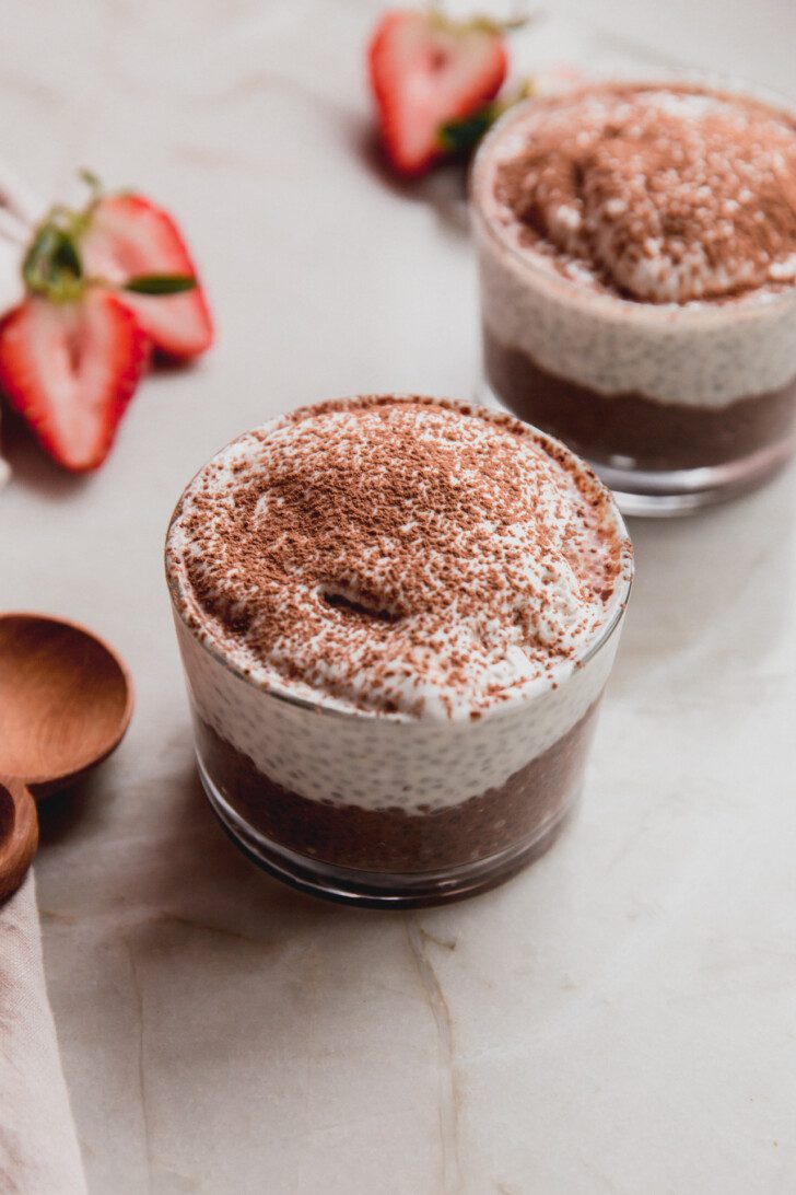 Tiramisu chia pudding in a small glass with fruit in the background.
