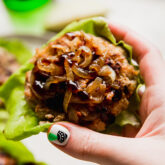 Person holding an apple chicken burger on lettuce.