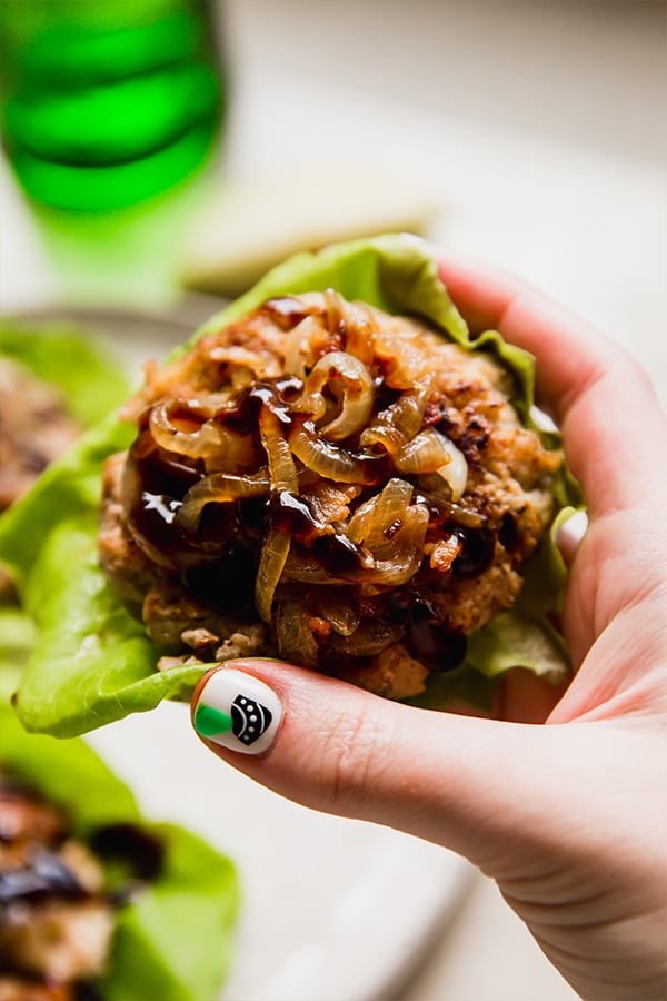 A apple chicken burger wrapped in lettuce being held in a hand.