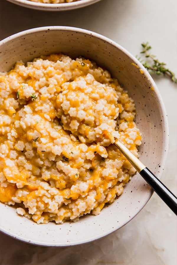 A bowl of butternut squash stelline with a spoon in it.