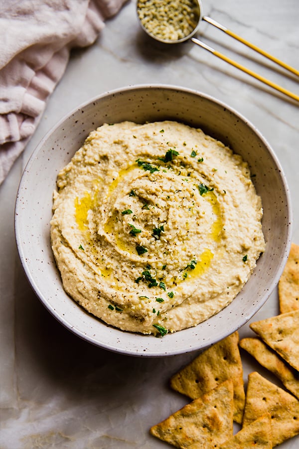 A bowl of hemp heart hummus with crackers on a counter.