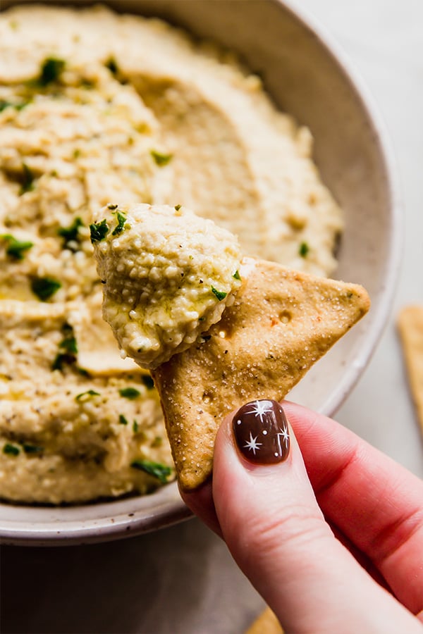 A cracker being dipped into hemp heart hummus.