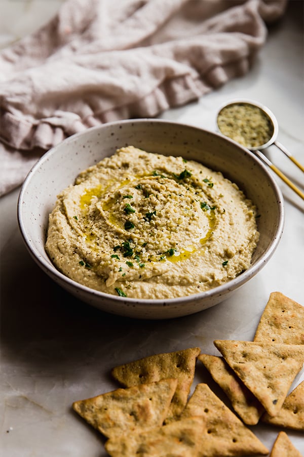 A bowl of hemp heart hummus on a counter with crackers nearby.