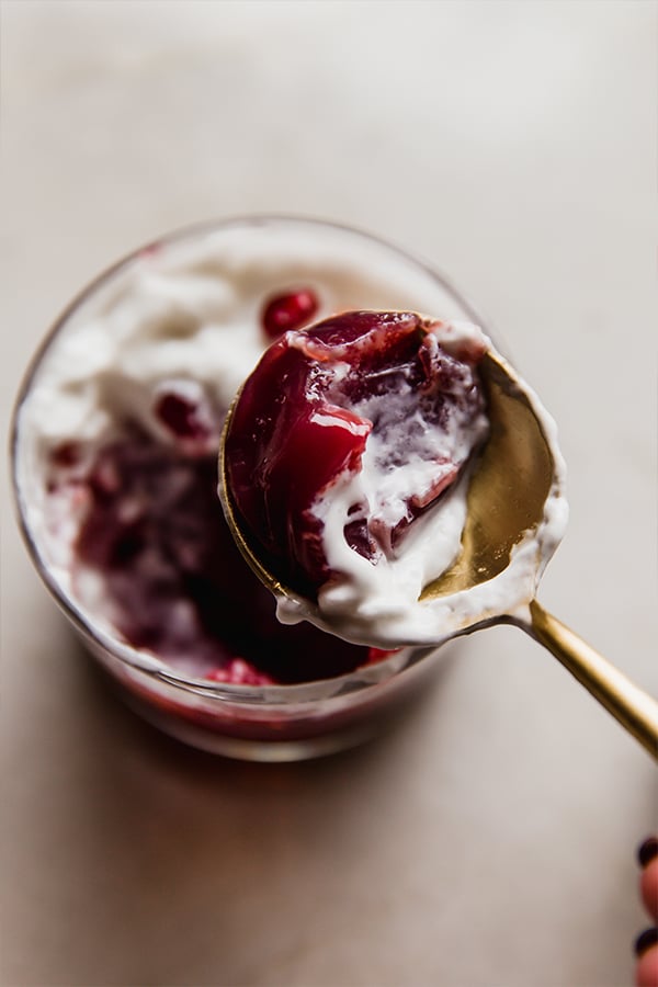 A spoon taking a bite of pomegranate jello topped with coconut cream.