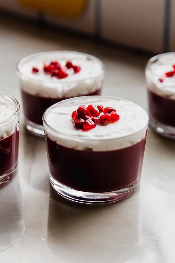 A few cups of pomegranate jello topped with coconut cream on a counter.